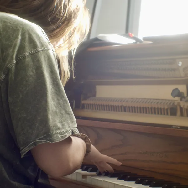 Violet Love at an upright piano in afternoon light, one hand resting on the keys.